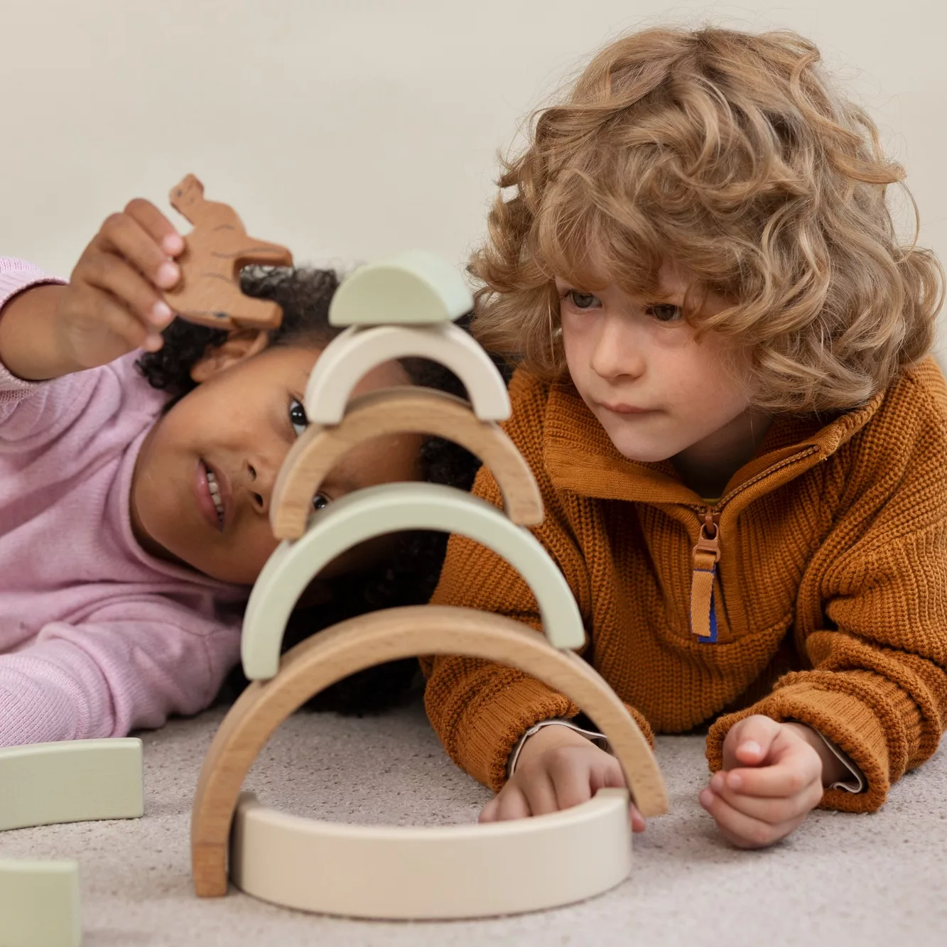 Enfants jouant avec un jeu d’arches en bois Montessori Deux enfants concentrés construisent une structure avec des arches en bois aux tons naturels et pastel, un jeu inspiré de la pédagogie Montessori favorisant la motricité fine, la créativité et la coordination main-œil.
